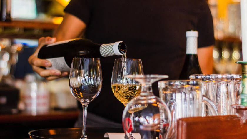 A person pouring wine into glasses at a bar.