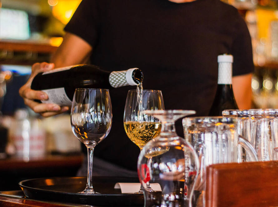 A person pouring wine into glasses at a bar.